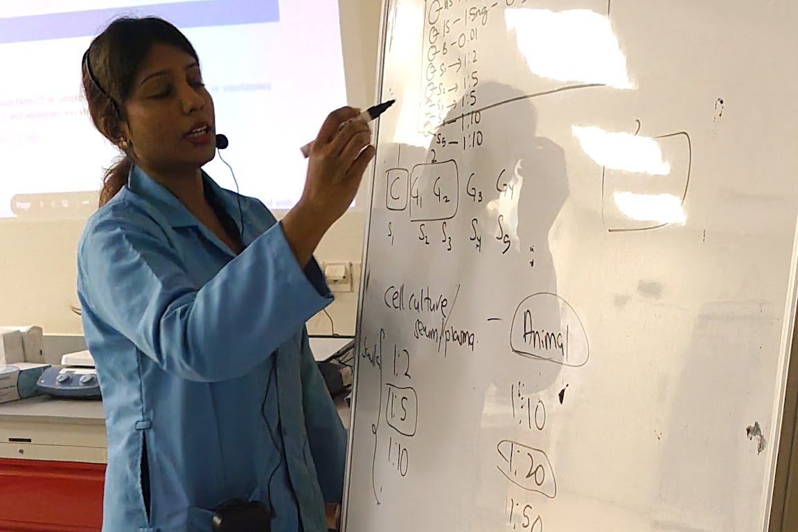 A trainer in a blue lab coat writes the steps on a whiteboard