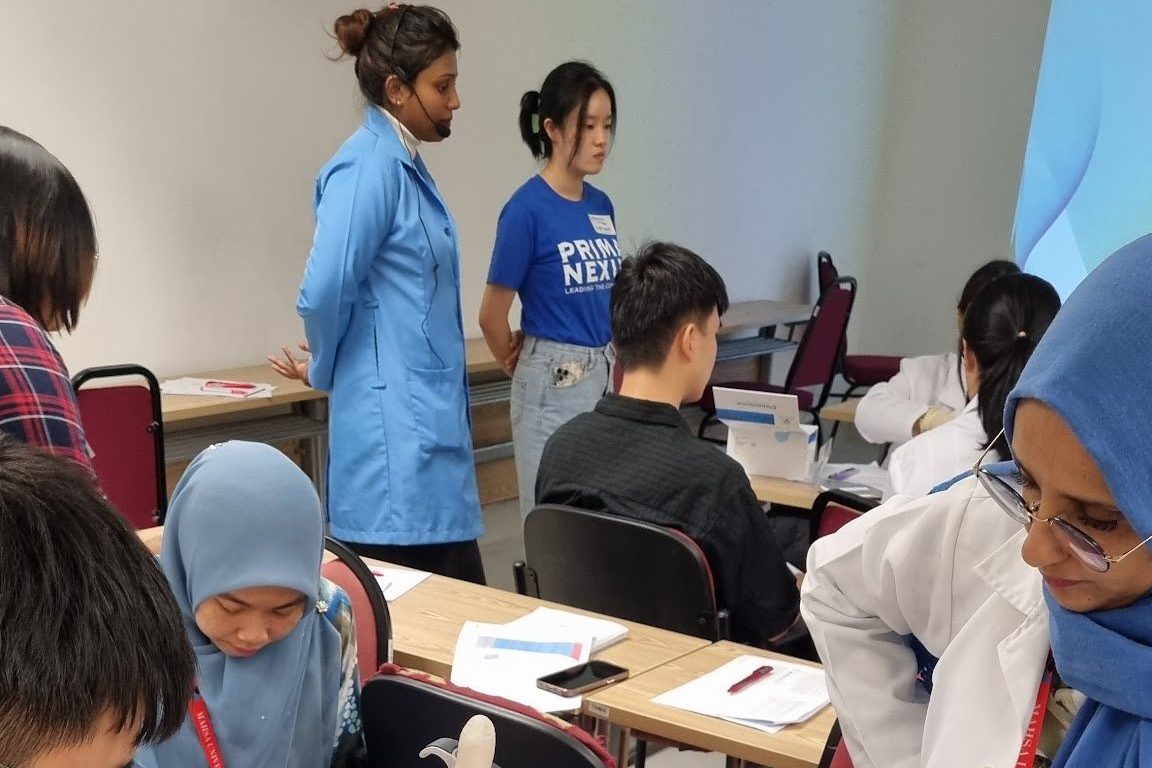 Participants at their tables handle the workshop materials while trainers in blue lab coats look on