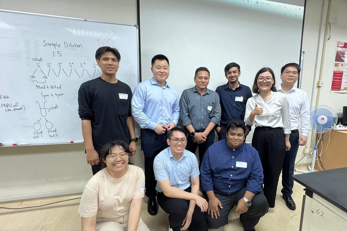 Participants and trainers standing and kneeling for a group photo in a laboratory, in front of a whiteboard
