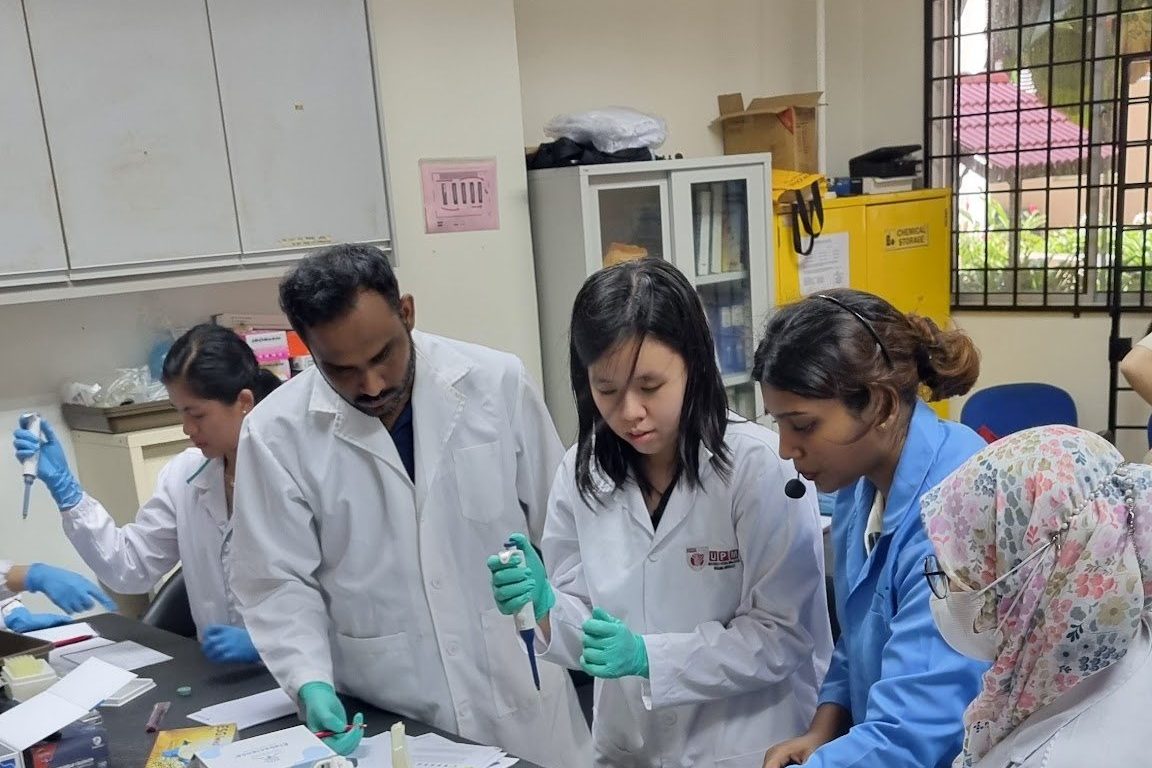 Participants in lab coats gather around a laboratory bench during the hands-on session