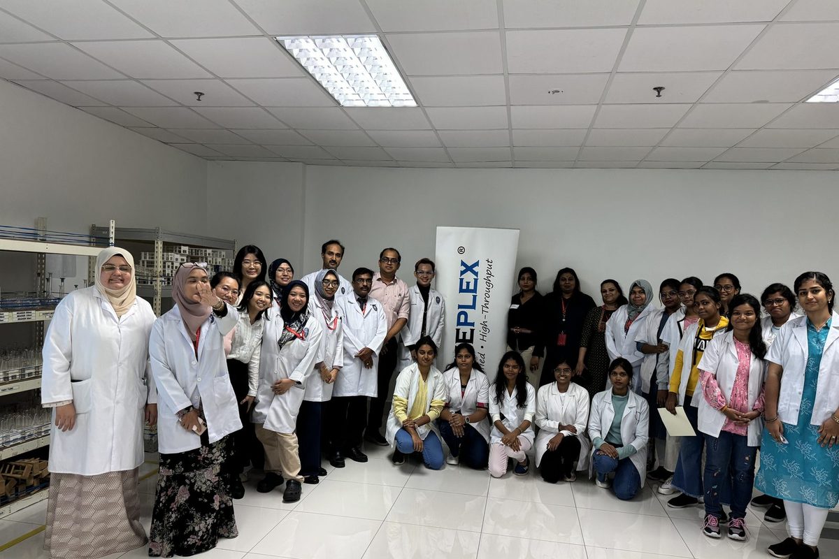 A large group of workshop participants in lab coats, standing and kneeling in a laboratory beside a PrimePlex banner
