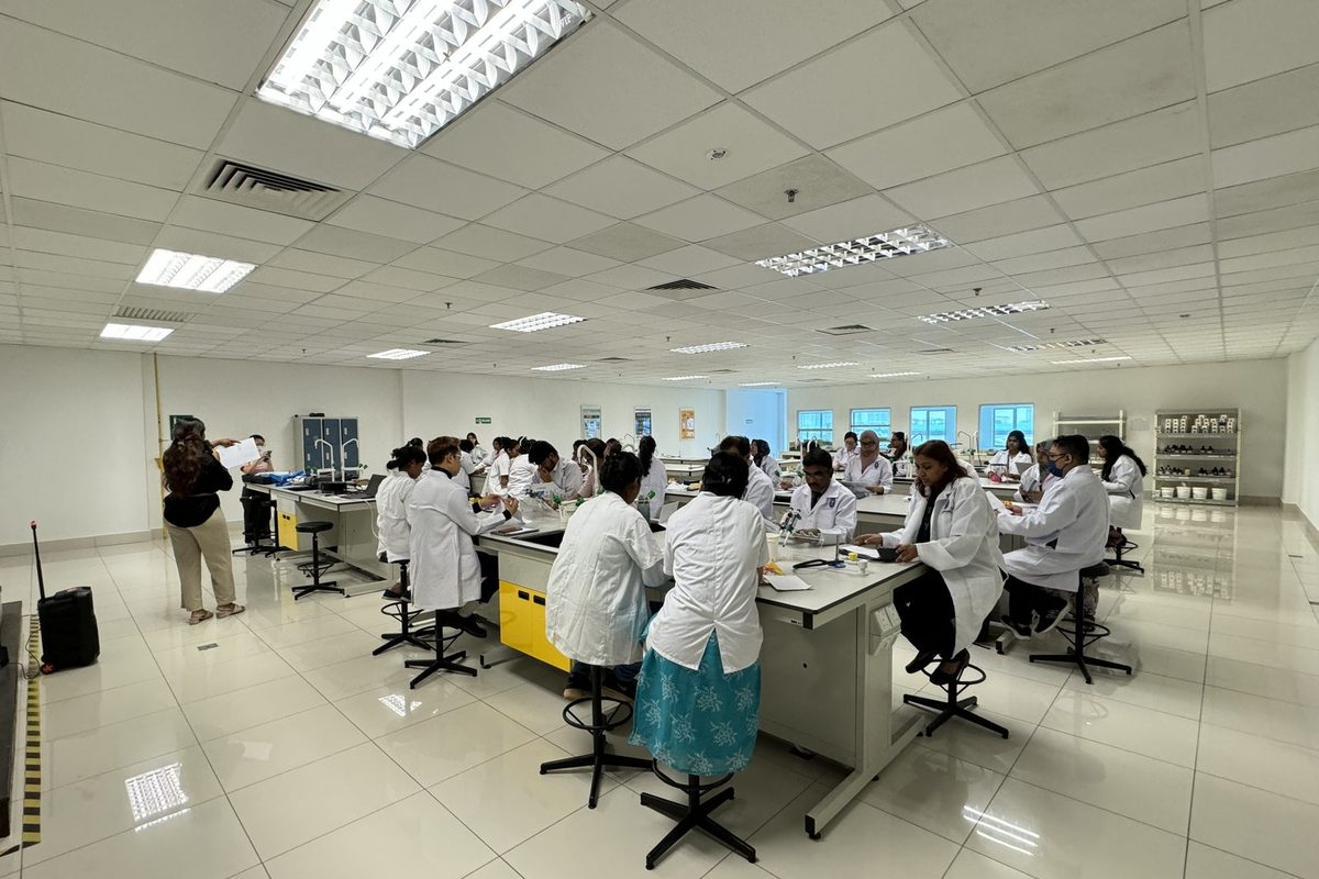 Participants in lab coats working in groups at benches across a large teaching laboratory