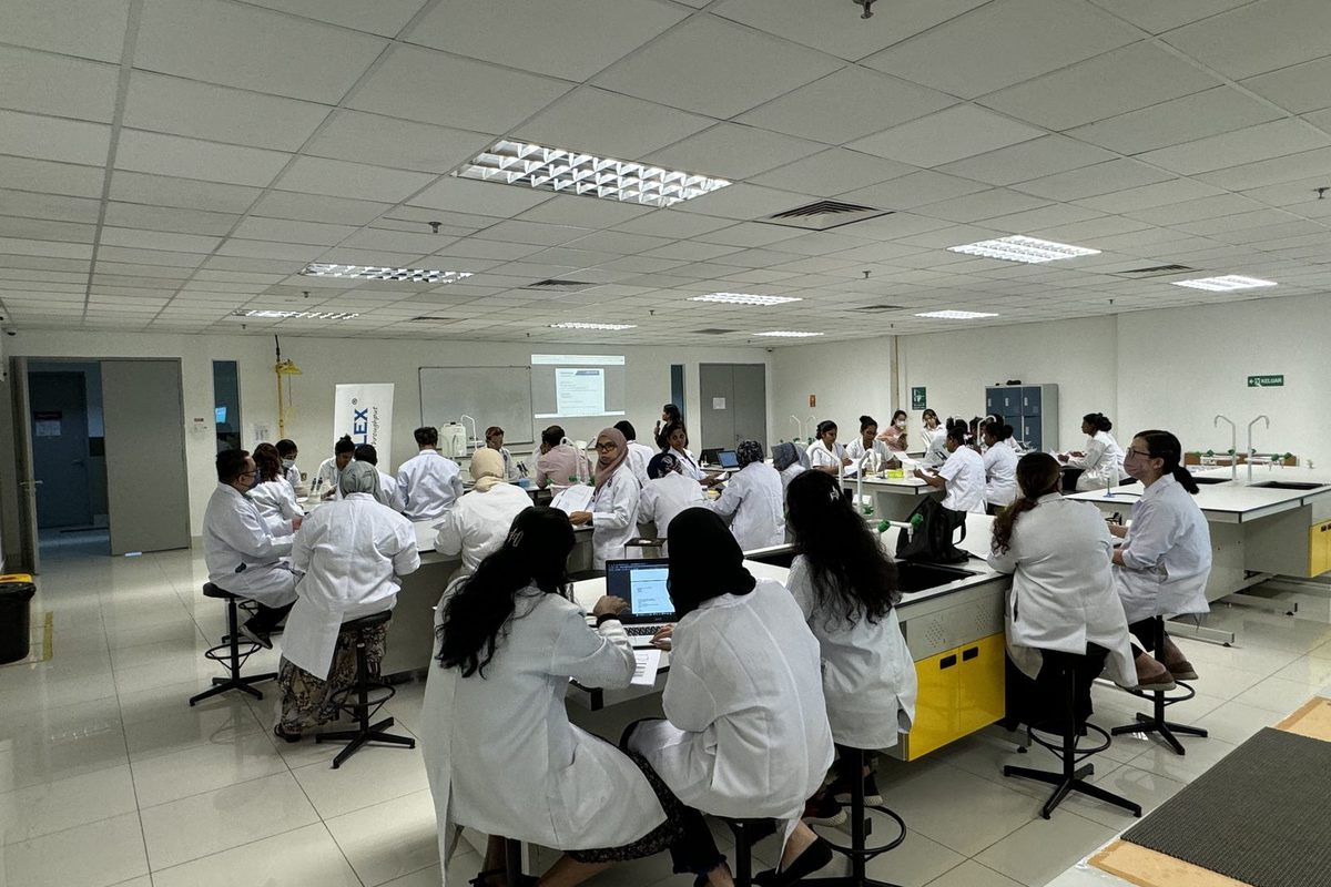 Participants in lab coats seated at a laboratory bench with a laptop, following the session