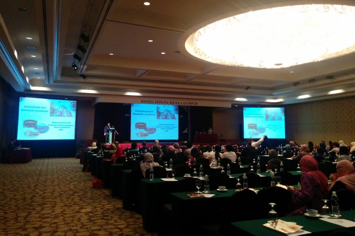 A speaker at the lectern, with her talk title on antioxidants and metabolic syndrome shown on three large screens