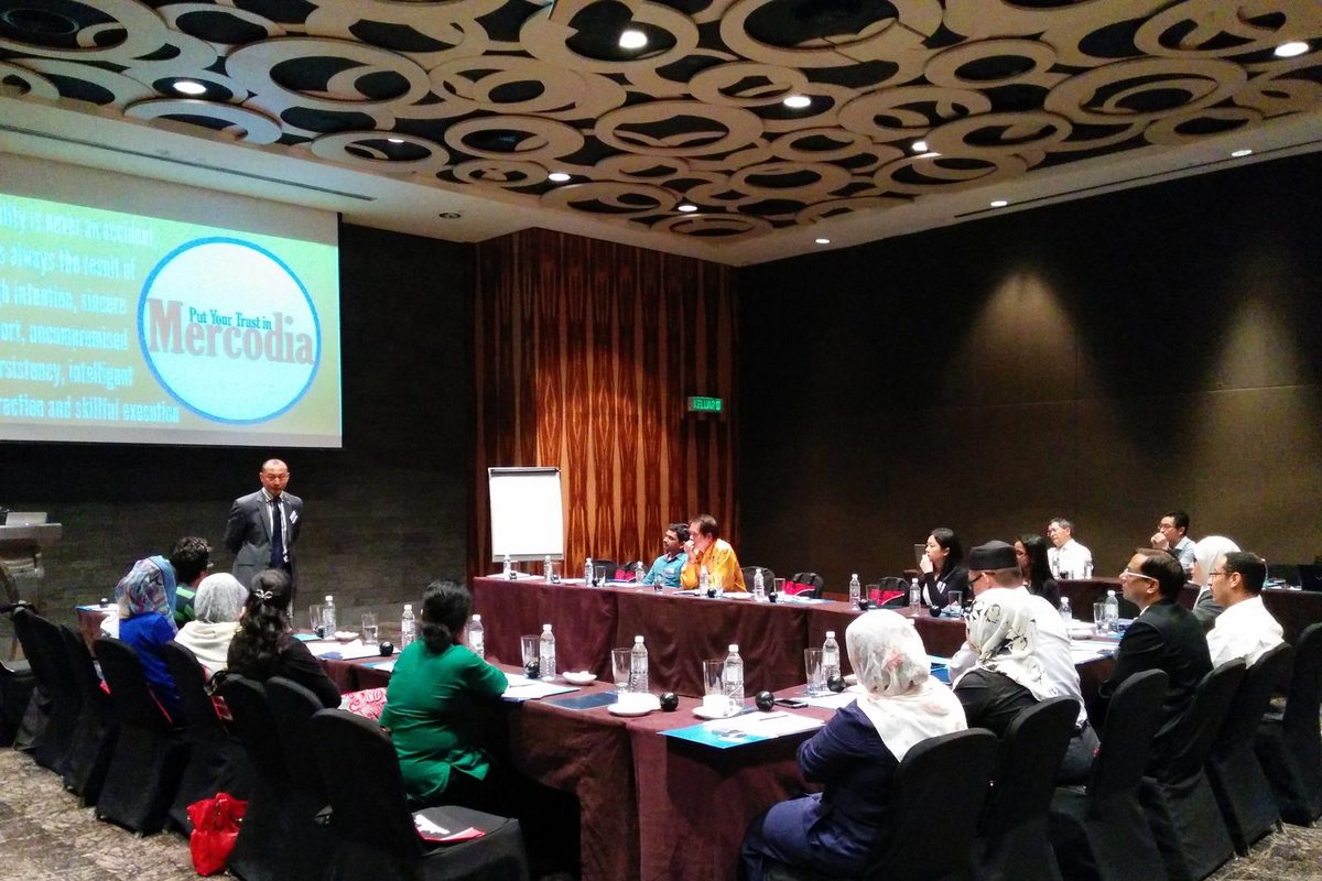 Speaker presents beside a Mercodia slide to participants seated at long tables in a hotel meeting room