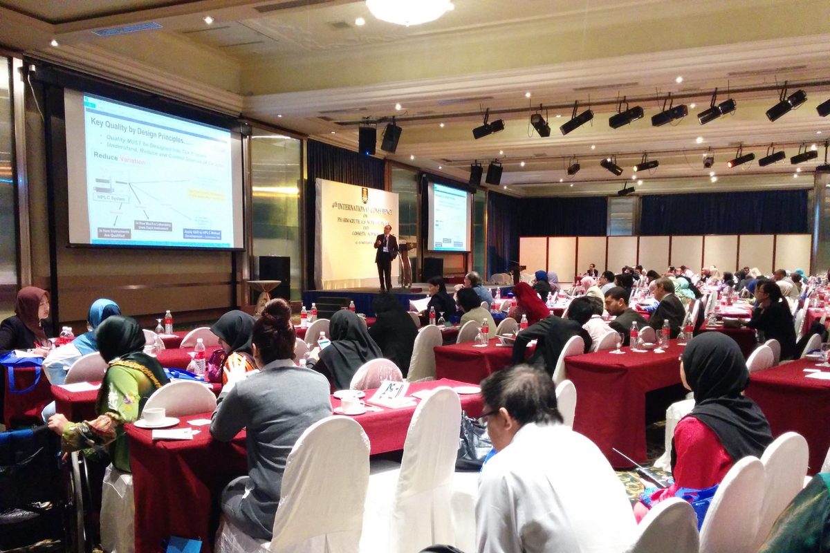 Delegates seated at round tables in the conference hall while a speaker presents from the front