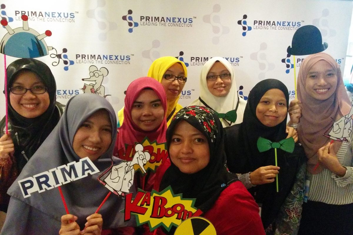 A group of delegates smiling and holding props in front of the Prima Nexus photo wall