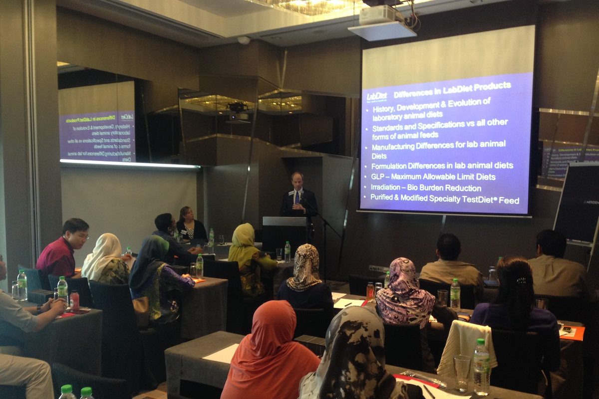A speaker at the lectern presents a slide on differences in LabDiet products to a seated audience