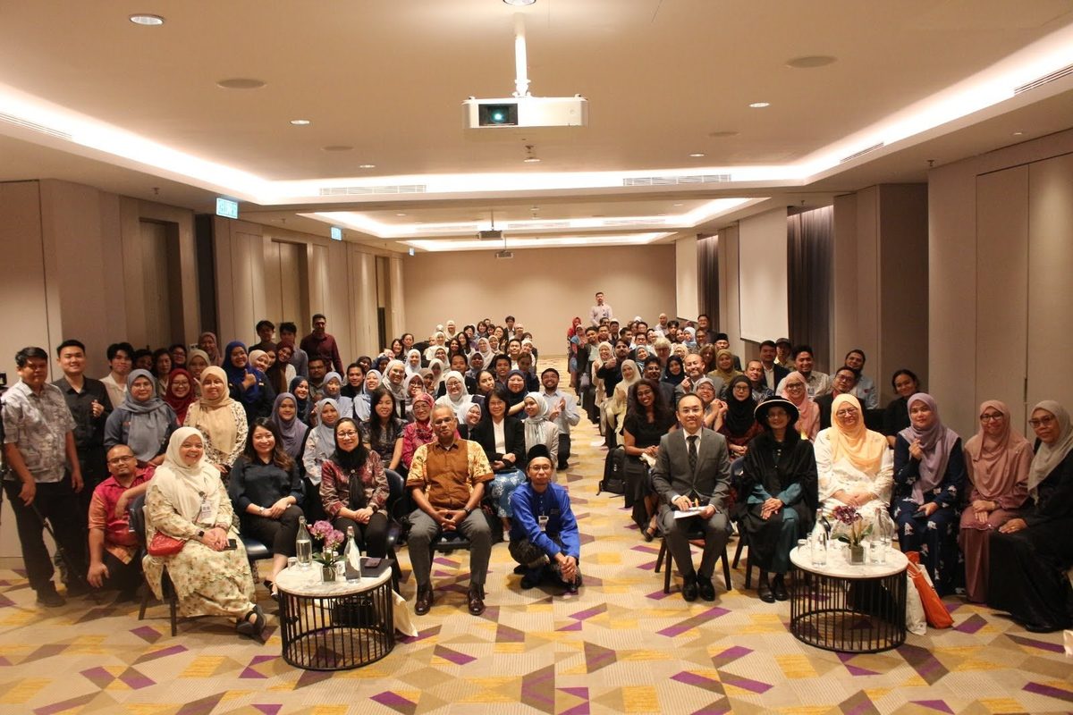 Group photo of more than a hundred guests in a hotel function room, with Prof. Dr Kalavathy Ramasamy in academic robes seated in the front row