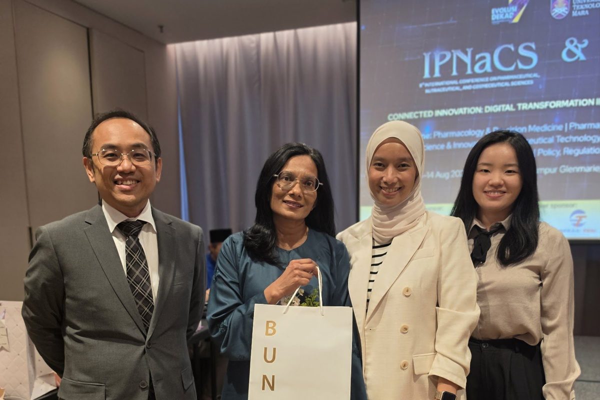 Four guests standing in front of the IPNaCS 2026 conference screen, among them Prima Nexus Managing Partner Nura Samsuddin