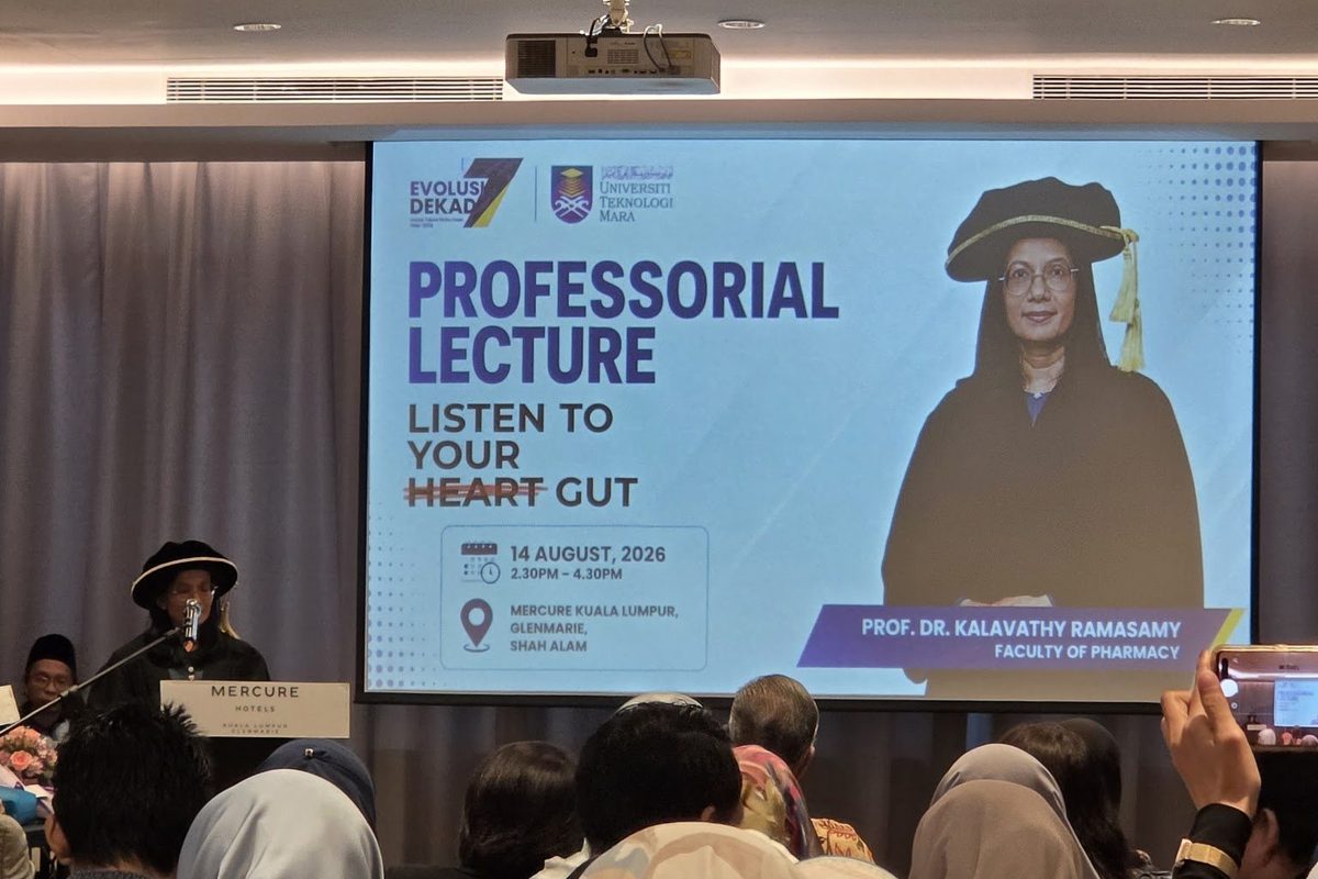 A speaker in academic cap and gown at the lectern beside a large screen showing the title slide Professorial Lecture, Listen to Your Gut