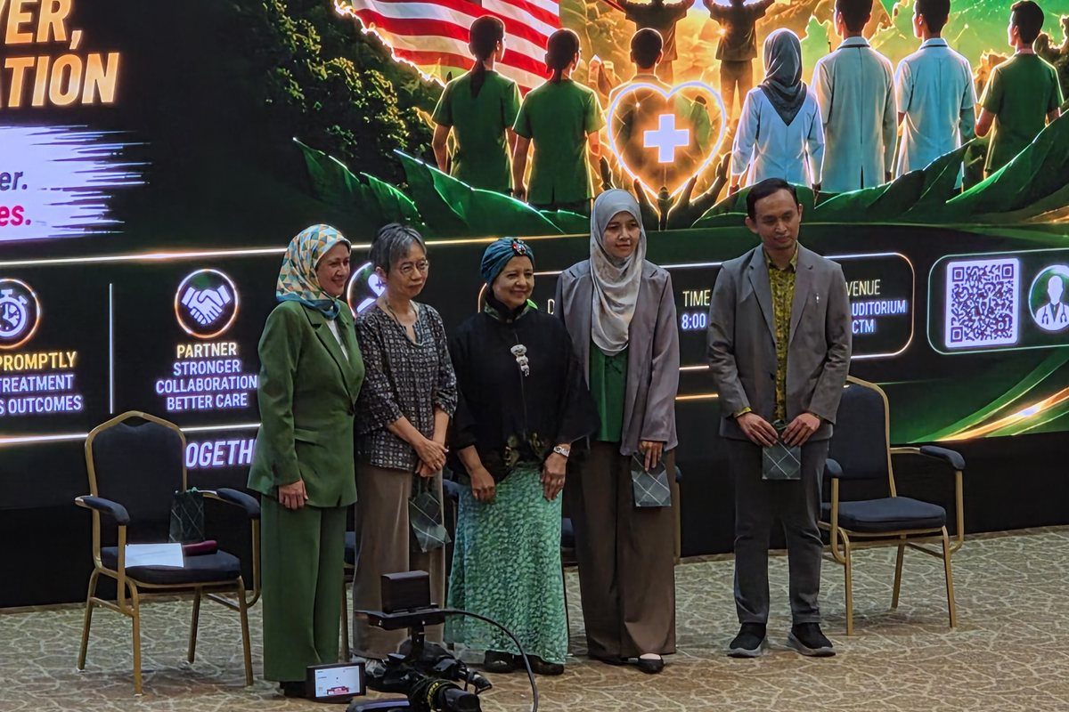 Five speakers standing on stage in front of a large green liver health screen in the HCTM auditorium