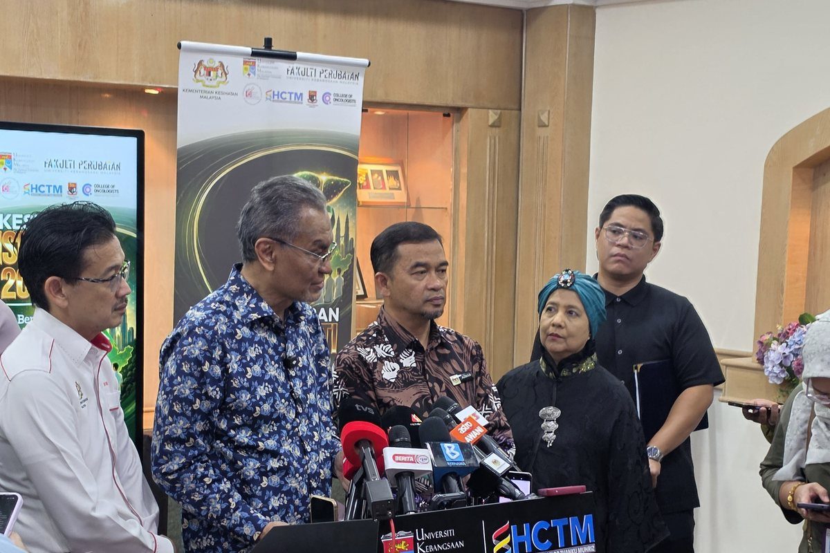 The Minister of Health speaking to reporters at a lectern with microphones, with Prof. Dato' Dr Rosmawati Mohamed standing nearby
