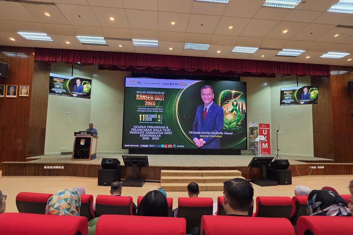 The Minister of Health speaking at the HCTM lectern, with a large screen announcing the launch of the National Liver Health Initiative roadmap 2026 to 2030