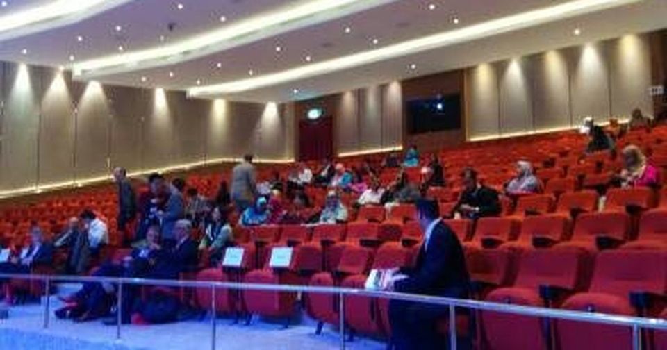 Delegates seated in the red-seat auditorium at Connexion@Nexus, seen from the side aisle