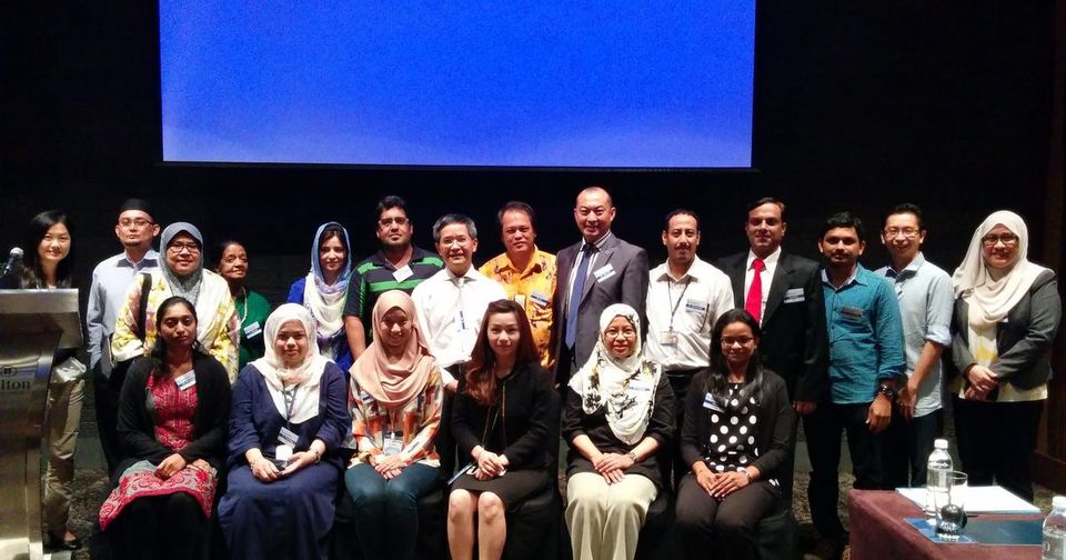 Group photo of participants standing and seated in front of the screen at Hilton Hotel, KL Sentral