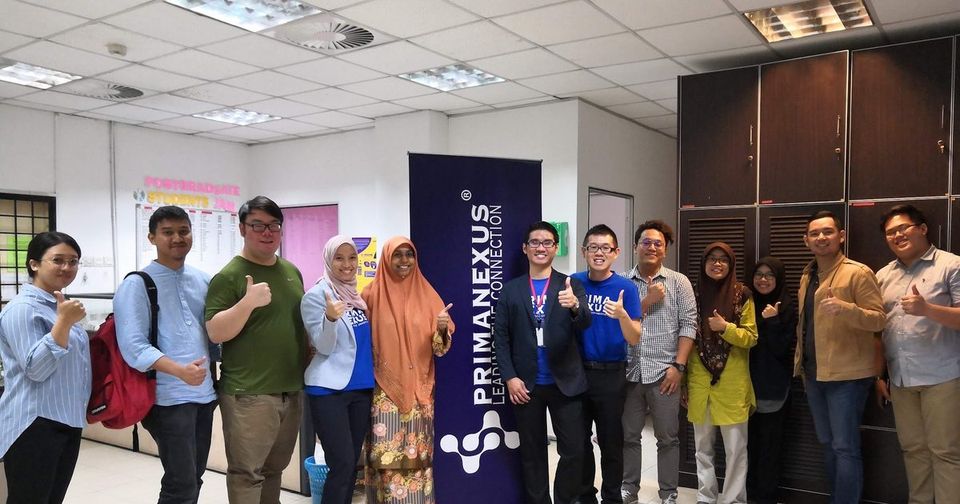 Workshop participants and trainers stand in a row at UPM, most of them giving a thumbs up