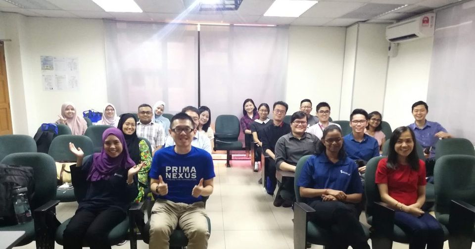 Workshop participants seated in rows of chairs in a lecture room, smiling and waving for the group photo
