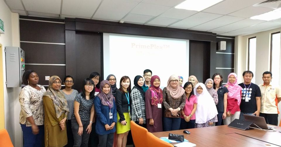 Participants and trainers stand for a group photo in the seminar room, with a title slide on the screen behind them