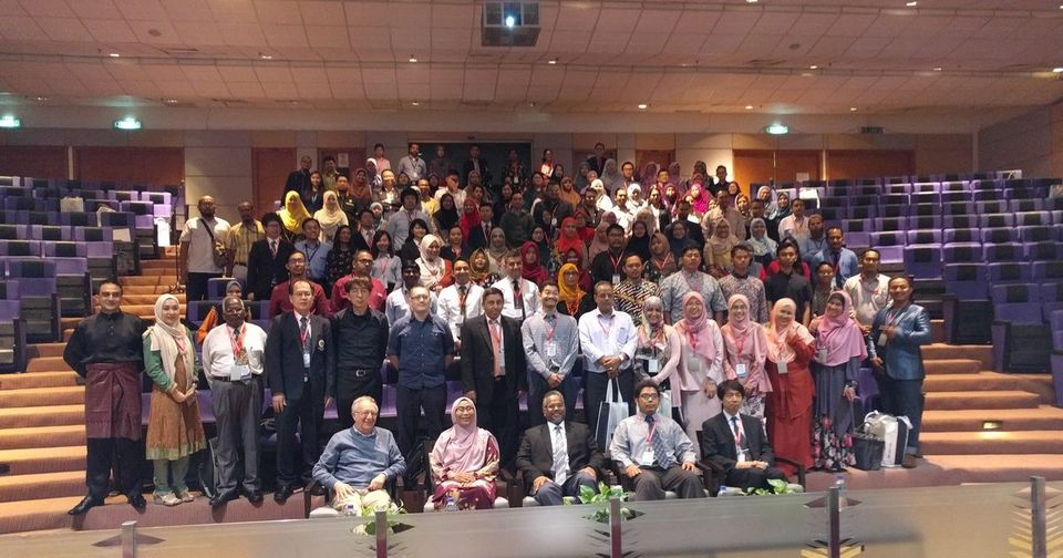 Large group photo of conference participants on the tiered seats of a lecture hall, front row seated