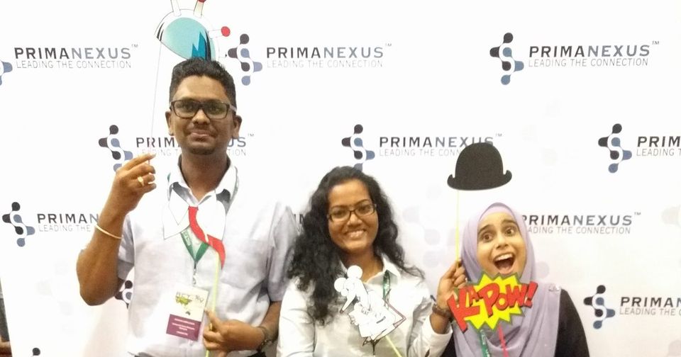 Three delegates pose with props in front of the Prima Nexus backdrop