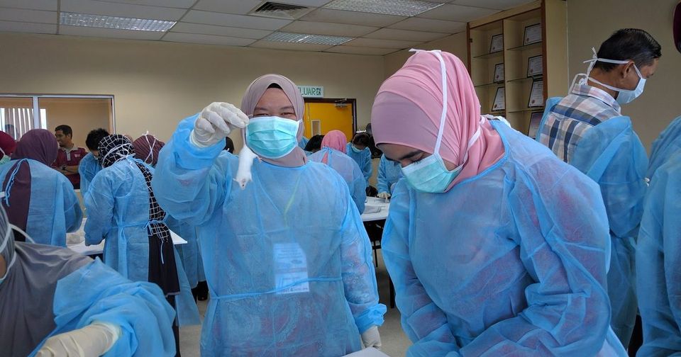 Participants in gowns, masks and gloves at the hands-on session; one holds up a white laboratory mouse
