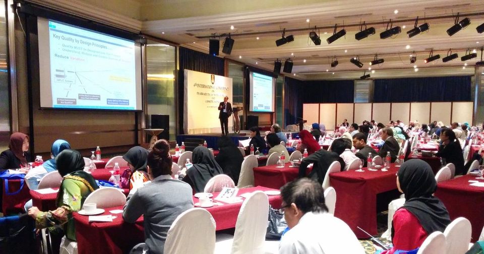 Delegates seated at round tables in the conference hall while a speaker presents from the front