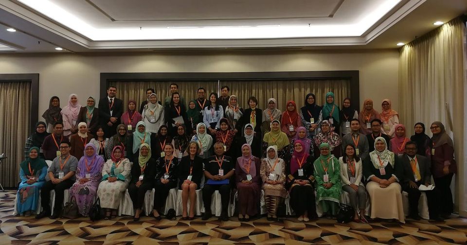 Large group photo of conference delegates, seated and standing in rows, in a hotel ballroom