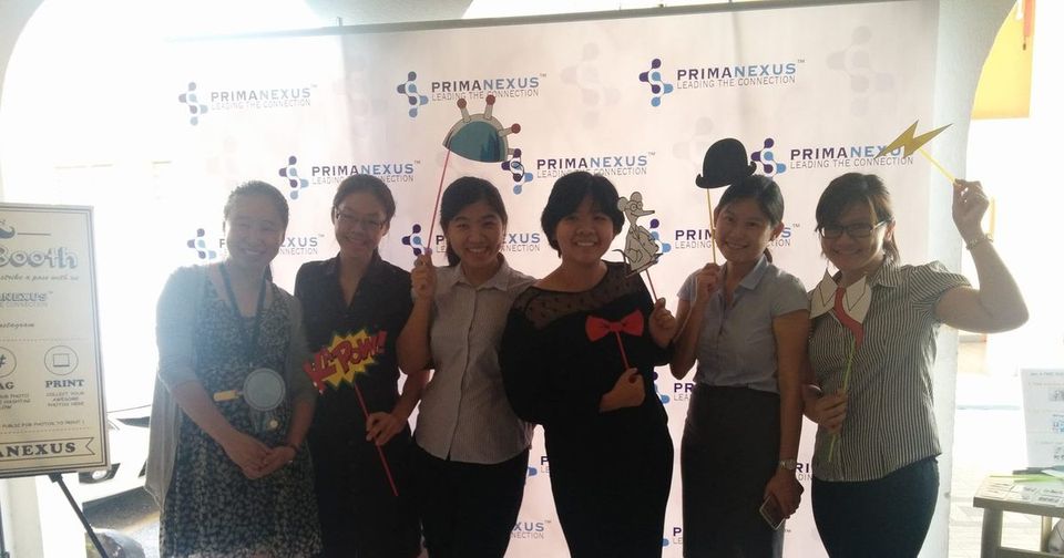 Six people holding photo props in front of the Prima Nexus logo backdrop