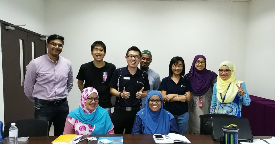 Workshop participants and trainers, two seated at a meeting table and the rest standing behind, smile for a group photo