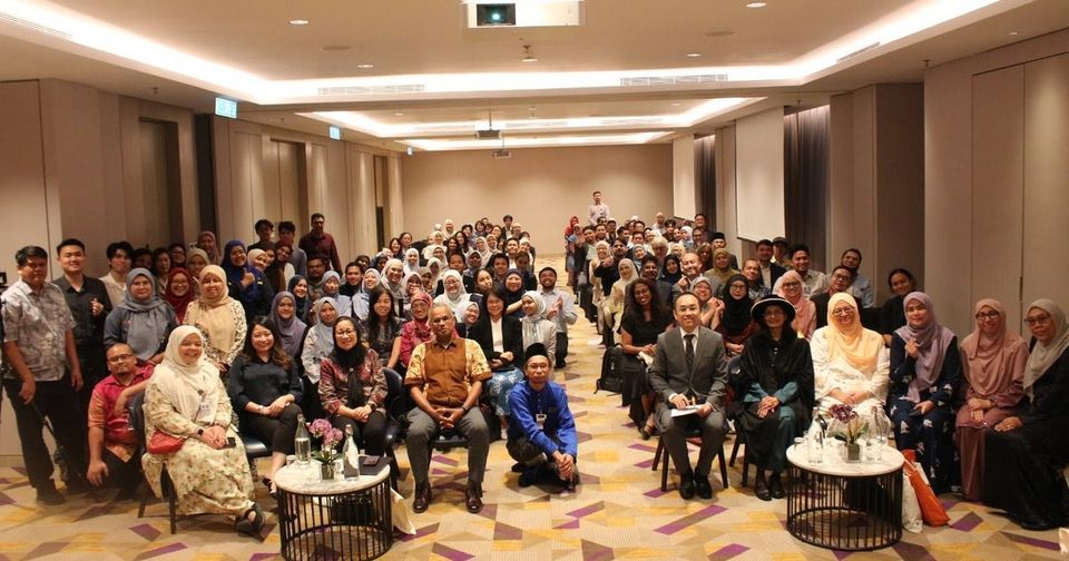 Group photo of more than a hundred guests in a hotel function room, with Prof. Dr Kalavathy Ramasamy in academic robes seated in the front row