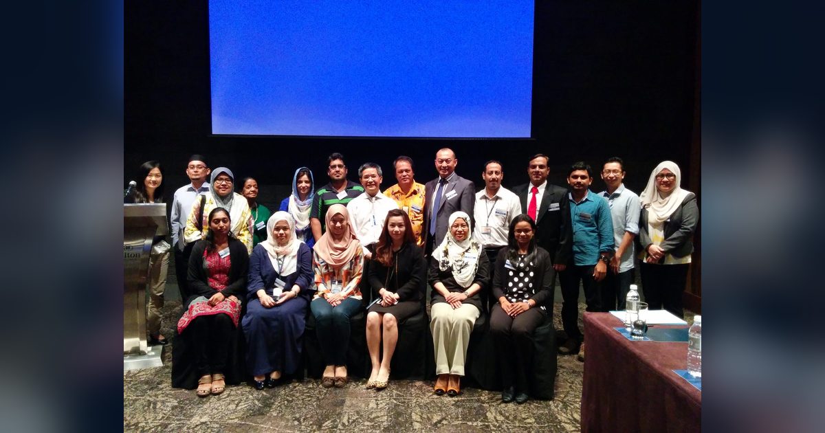 Group photo of participants standing and seated in front of the screen at Hilton Hotel, KL Sentral