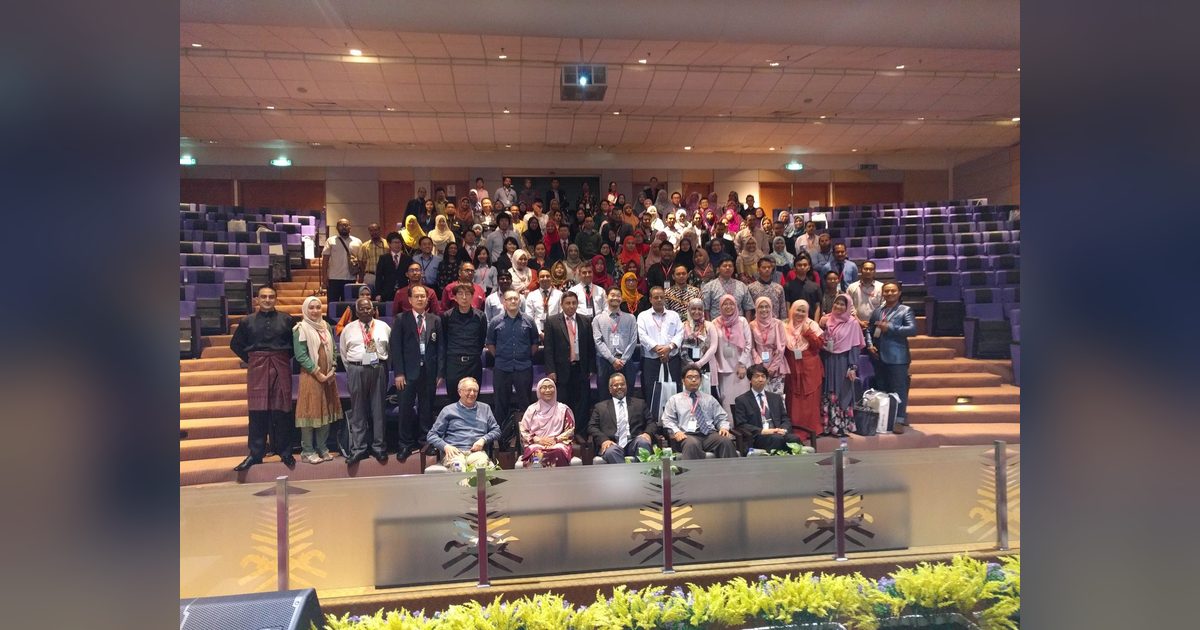 Large group photo of conference participants on the tiered seats of a lecture hall, front row seated