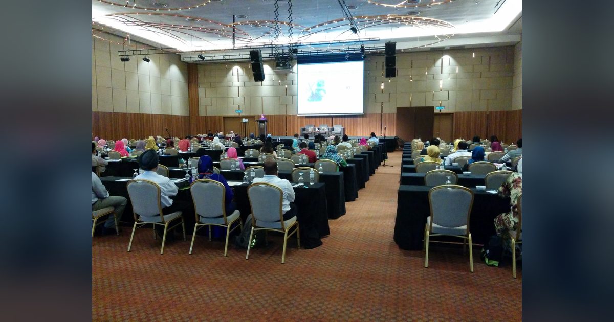 Delegates seated at rows of long tables in the ballroom, facing the stage and a large screen