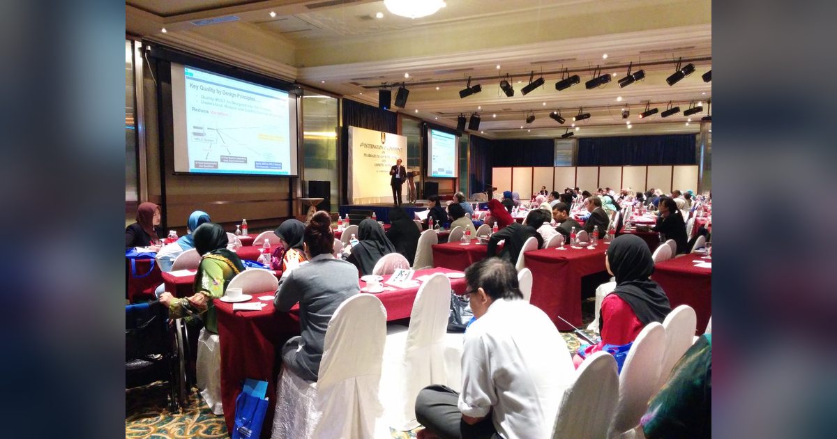 Delegates seated at round tables in the conference hall while a speaker presents from the front